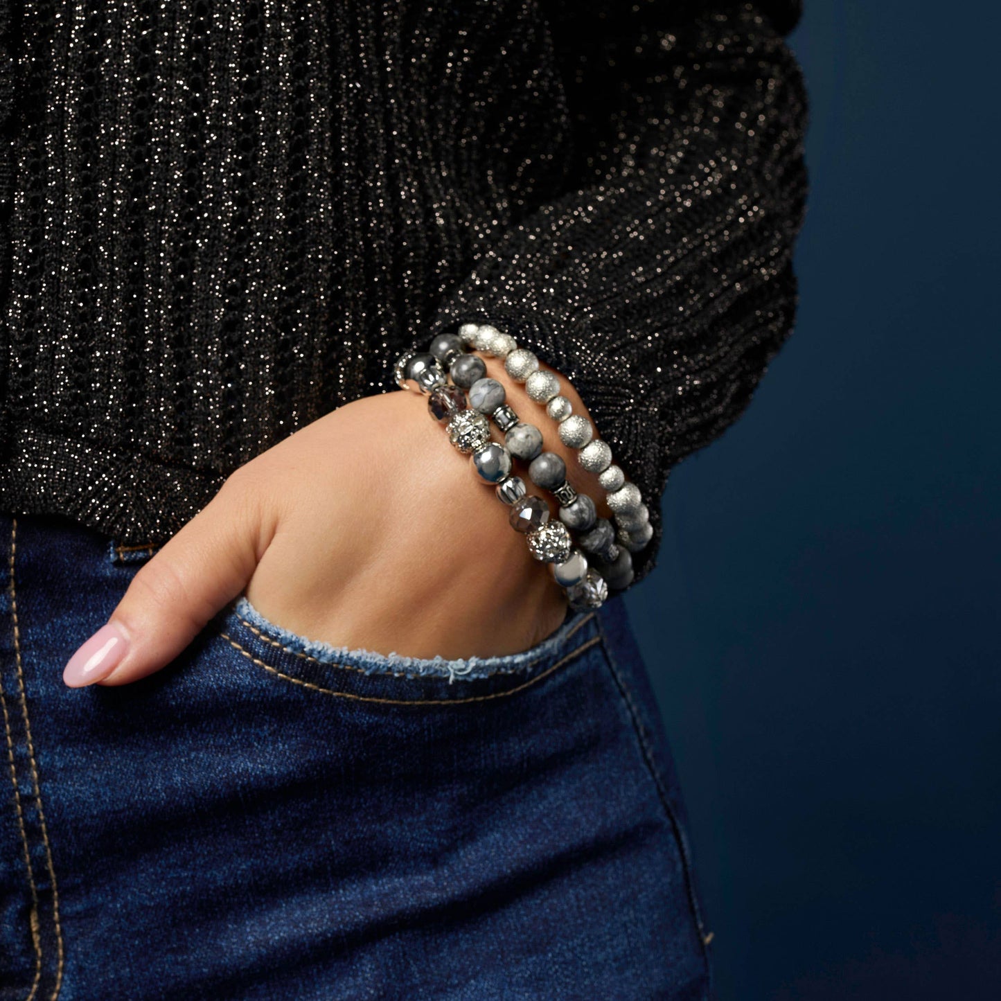 Hand wearing multiple bracelets with a dark background