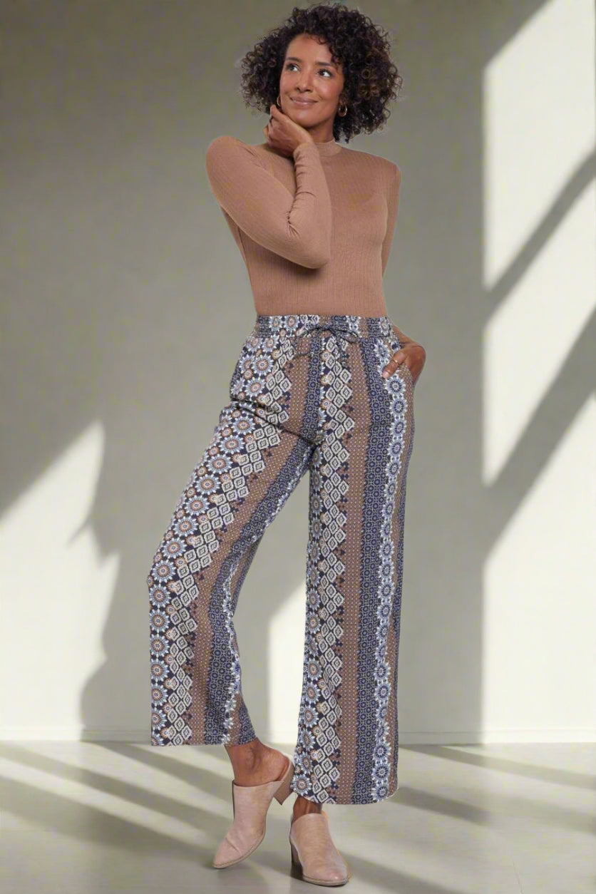 Woman wearing a beige top and patterned pants on a white background