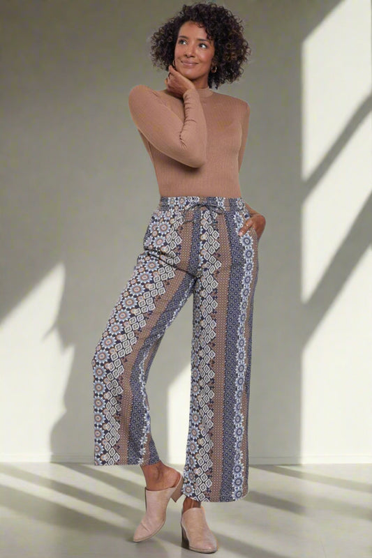 Woman wearing a beige top and patterned pants on a white background