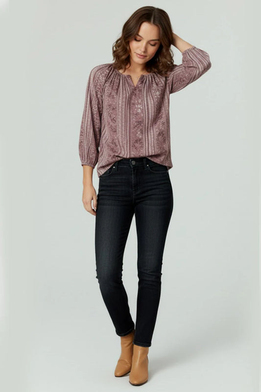 Woman wearing a patterned blouse, black jeans, and tan boots on a white background