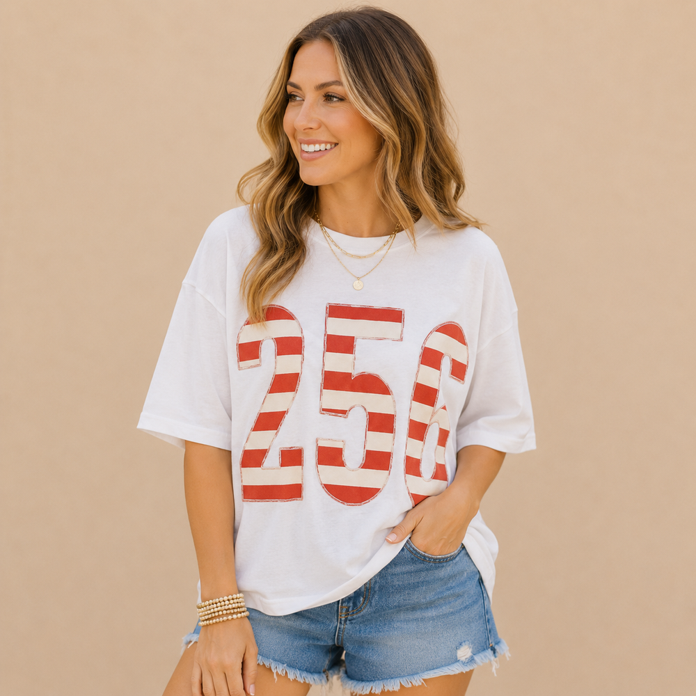 A woman wearing a white oversized graphic T-shirt with large red and white striped '250' lettering, paired with distressed denim shorts, posed against a solid beige background.