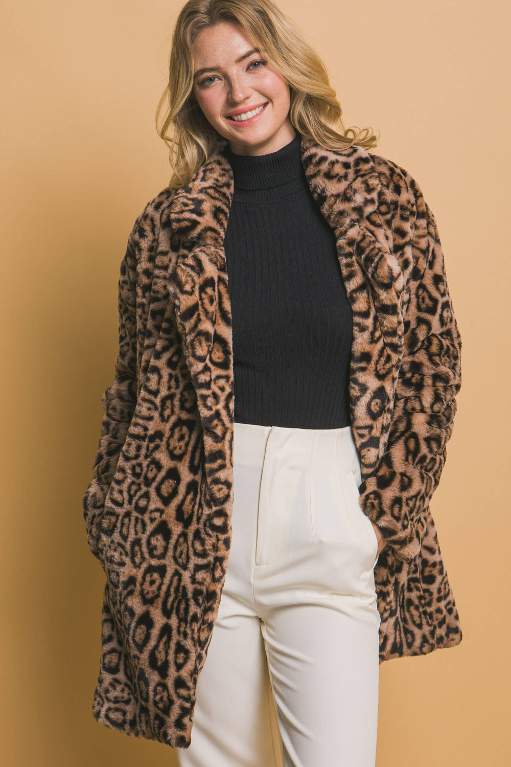 Woman wearing a leopard print coat over a black top and white pants on a beige background