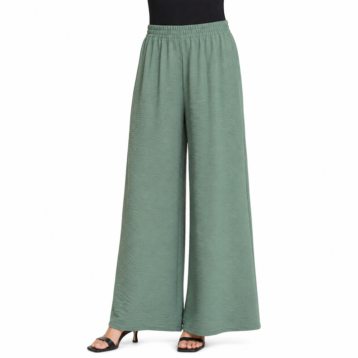 A person modeling wide-leg sage green pants with an elastic waistband, paired with black heeled sandals against a plain white background.