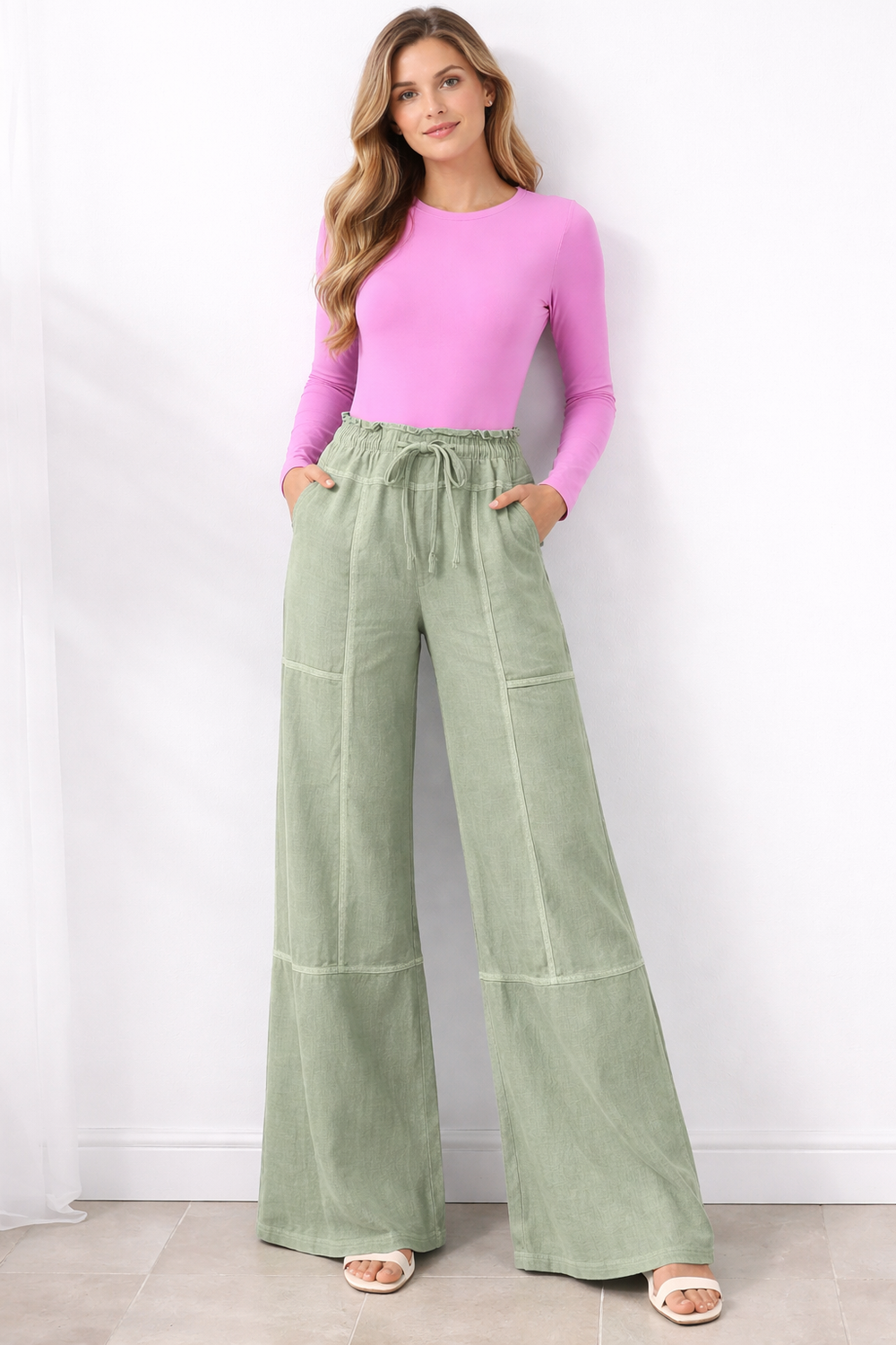 Woman wearing a pink top and green wide-leg pants against a white background