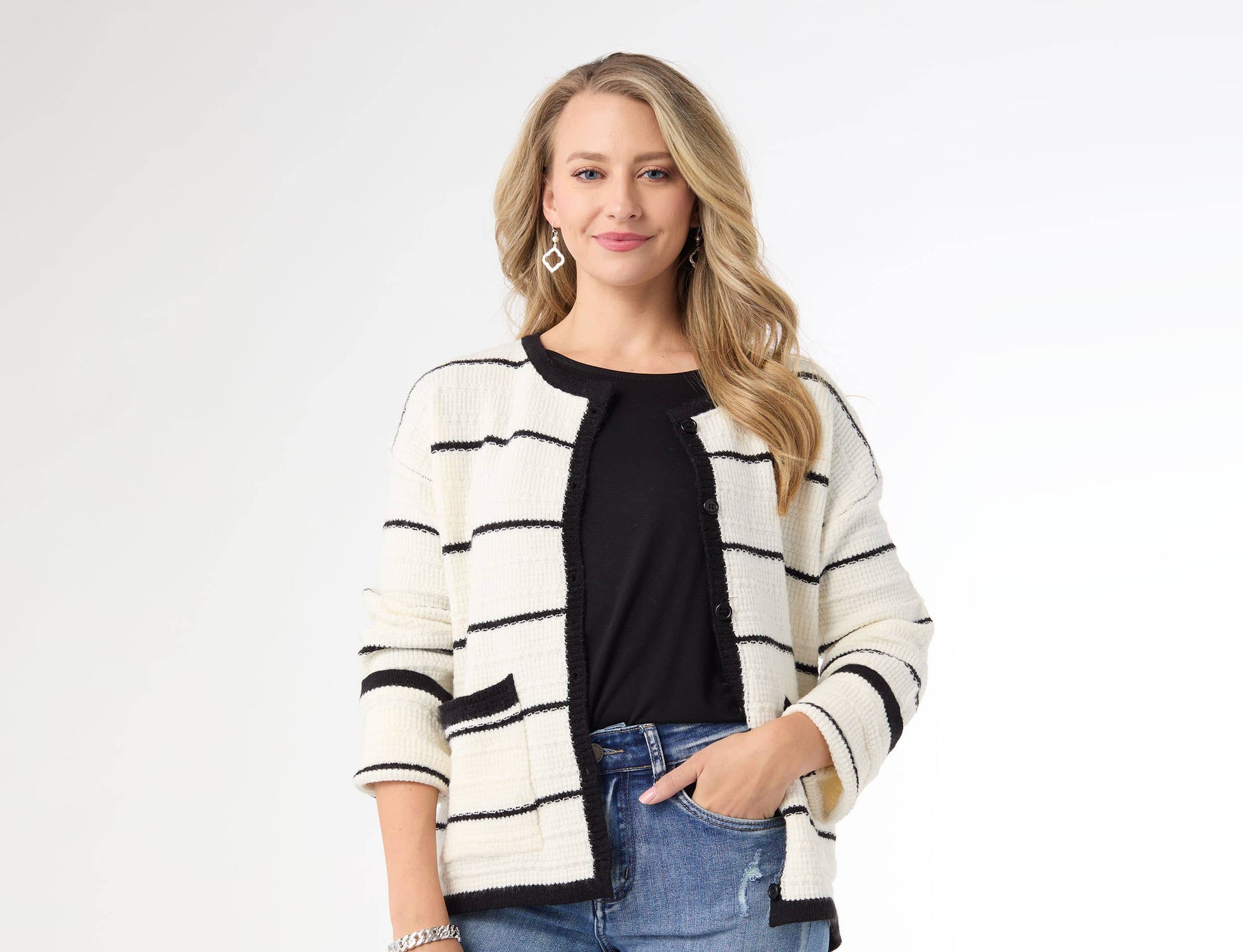 Woman wearing a black and white striped cardigan over a black top and blue jeans on a white background
