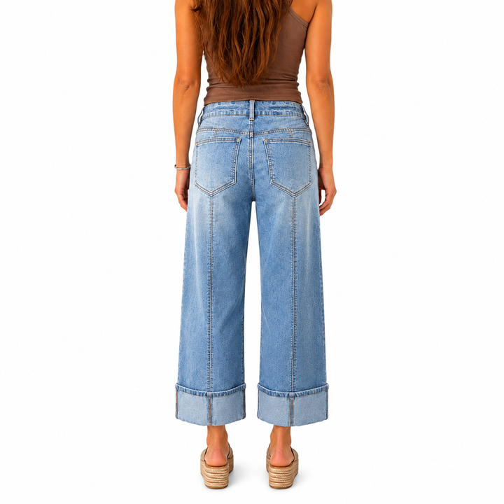 A woman shown from the back wearing light-wash wide-leg cropped jeans with rolled cuffs, a brown sleeveless top, and tan wedge sandals against a plain white background.