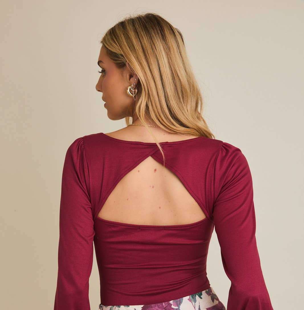 Woman wearing a burgundy long-sleeve top with cut-out design on a beige background