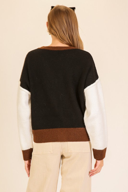Person wearing a black, white, and brown sweater with beige pants on a beige background