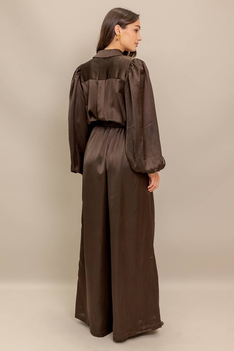 Woman wearing a brown satin jumpsuit on a beige background