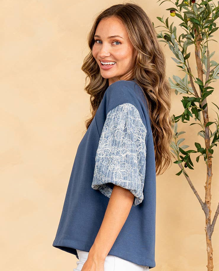 Woman wearing a blue top with lace sleeves against a beige background