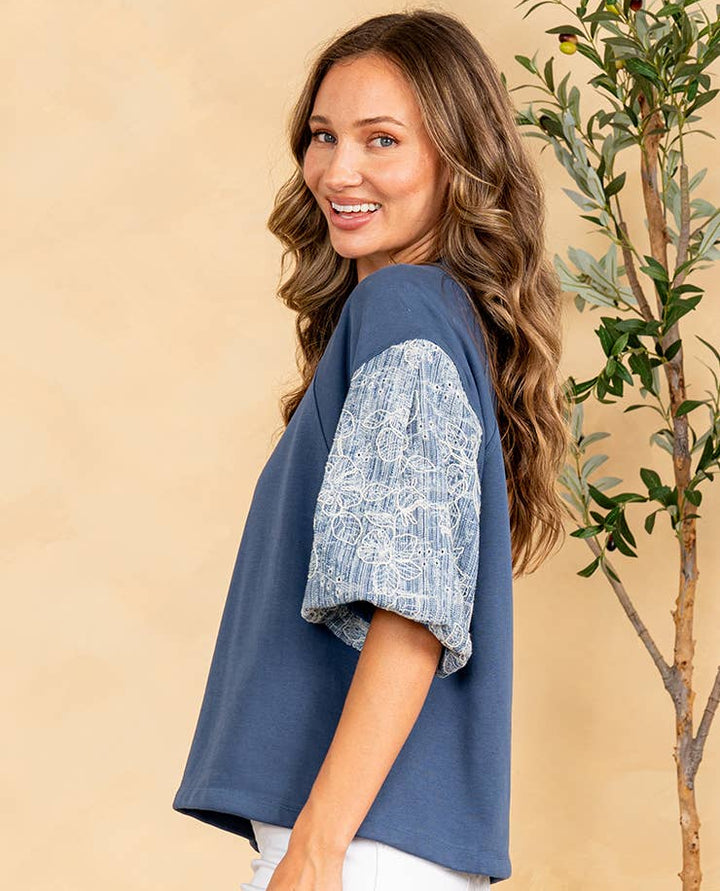 Woman wearing a blue top with lace sleeves against a beige background