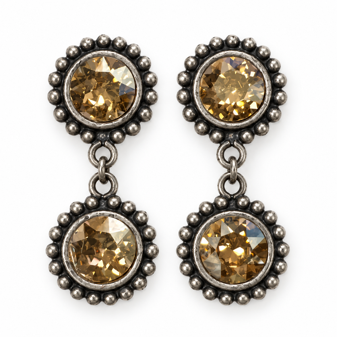 A pair of drop earrings with round faceted amber-brown gemstones in oxidized silver-toned settings, featuring a beaded border and a small dangling bead chain between the two round settings.