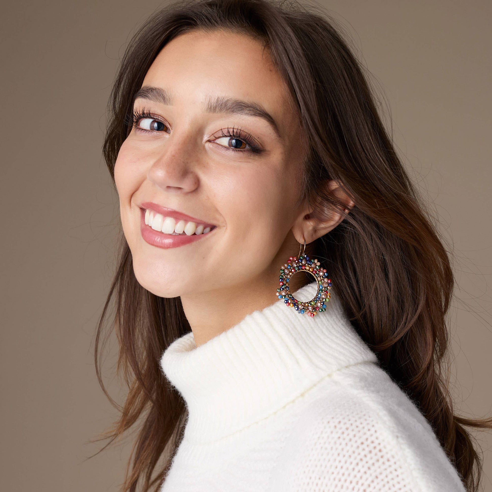 Woman wearing colorful earrings with a neutral background