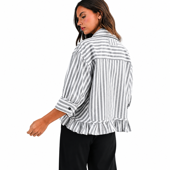 A woman wearing an ash black and white vertically striped ruffled blouse with rolled-up sleeves, paired with black pants, shown from a side-back angle against a plain white background.