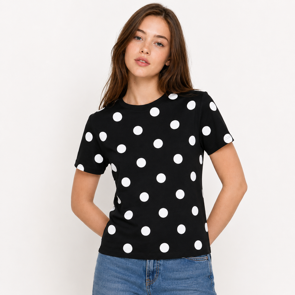 A woman wearing a black short-sleeve crewneck t-shirt with a white polka dot pattern, paired with blue jeans, photographed against a plain white studio background.