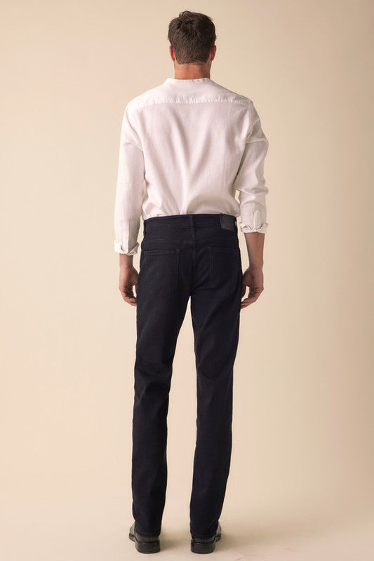 Man wearing a white shirt and dark pants against a beige background