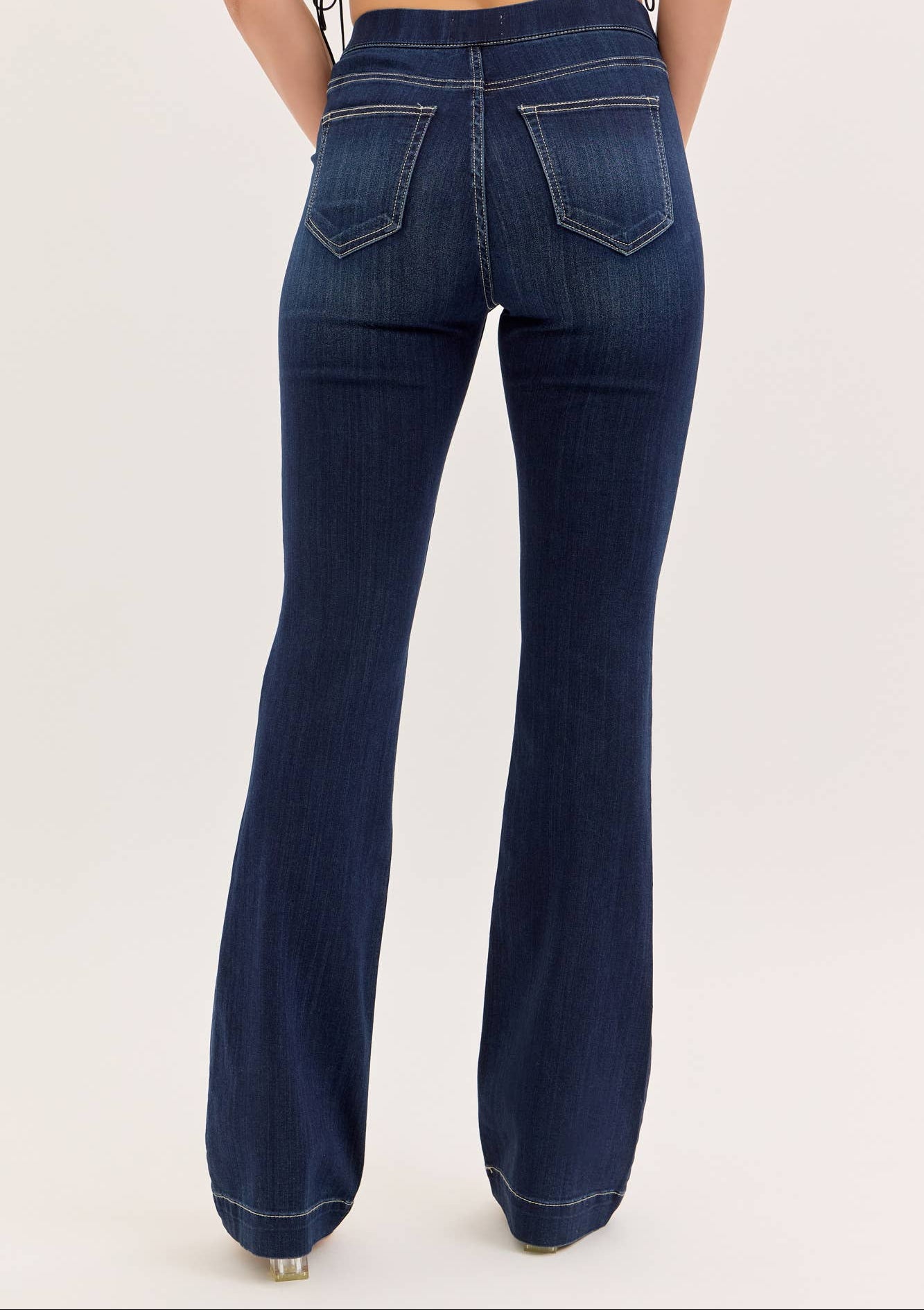 Dark blue flared jeans worn by a person on a light beige background