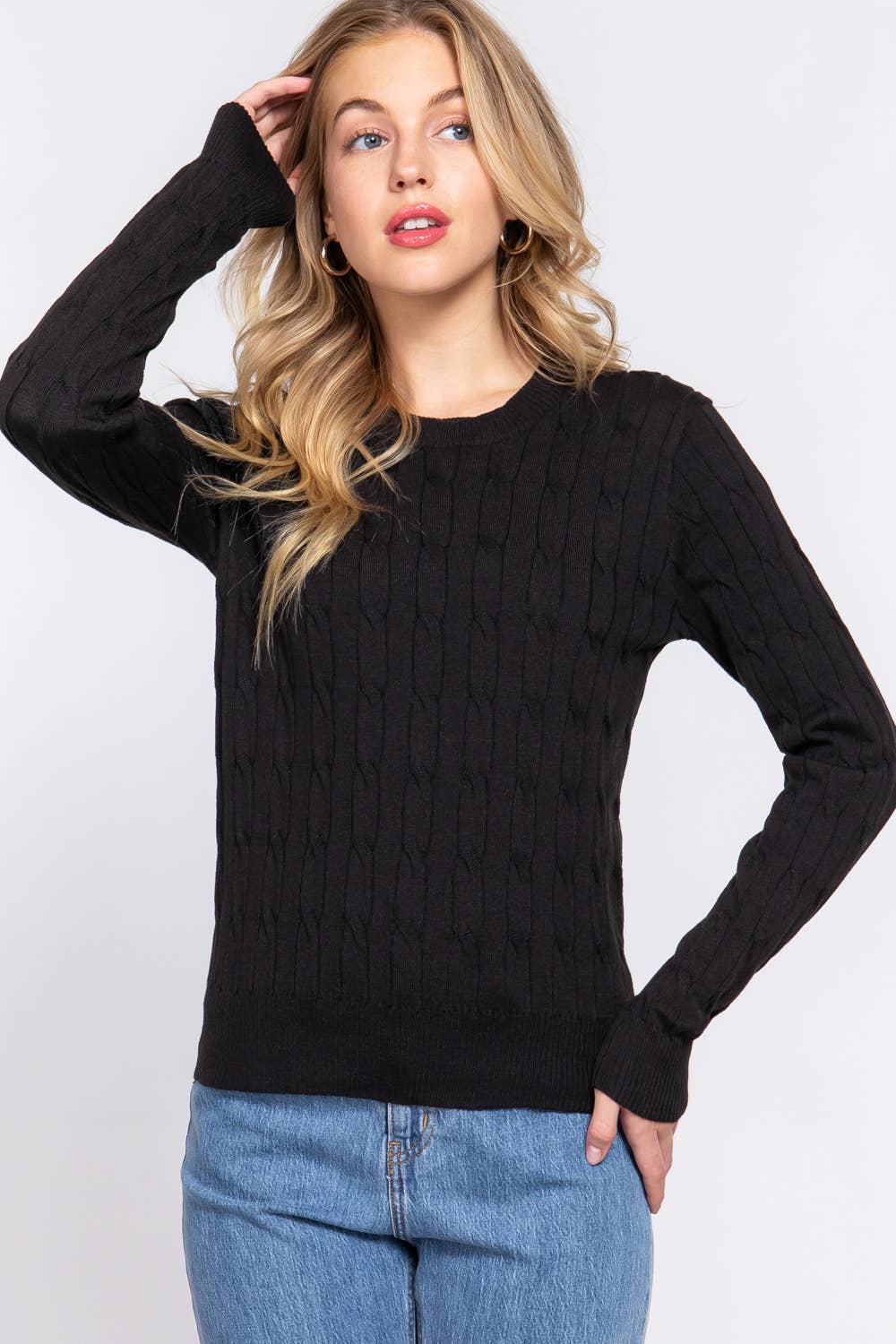 Woman wearing a black cable knit sweater and blue jeans on a white background