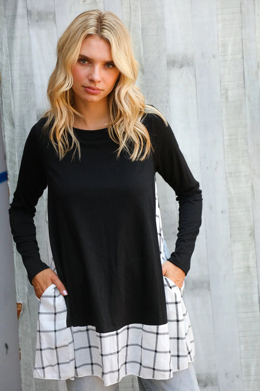 Woman wearing a black long-sleeve top with a white and black checkered skirt against a wooden wall.