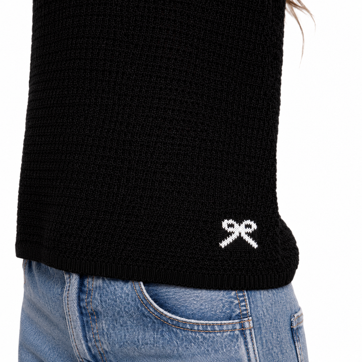 Black sweater with a white logo on the sleeve, worn with blue jeans.