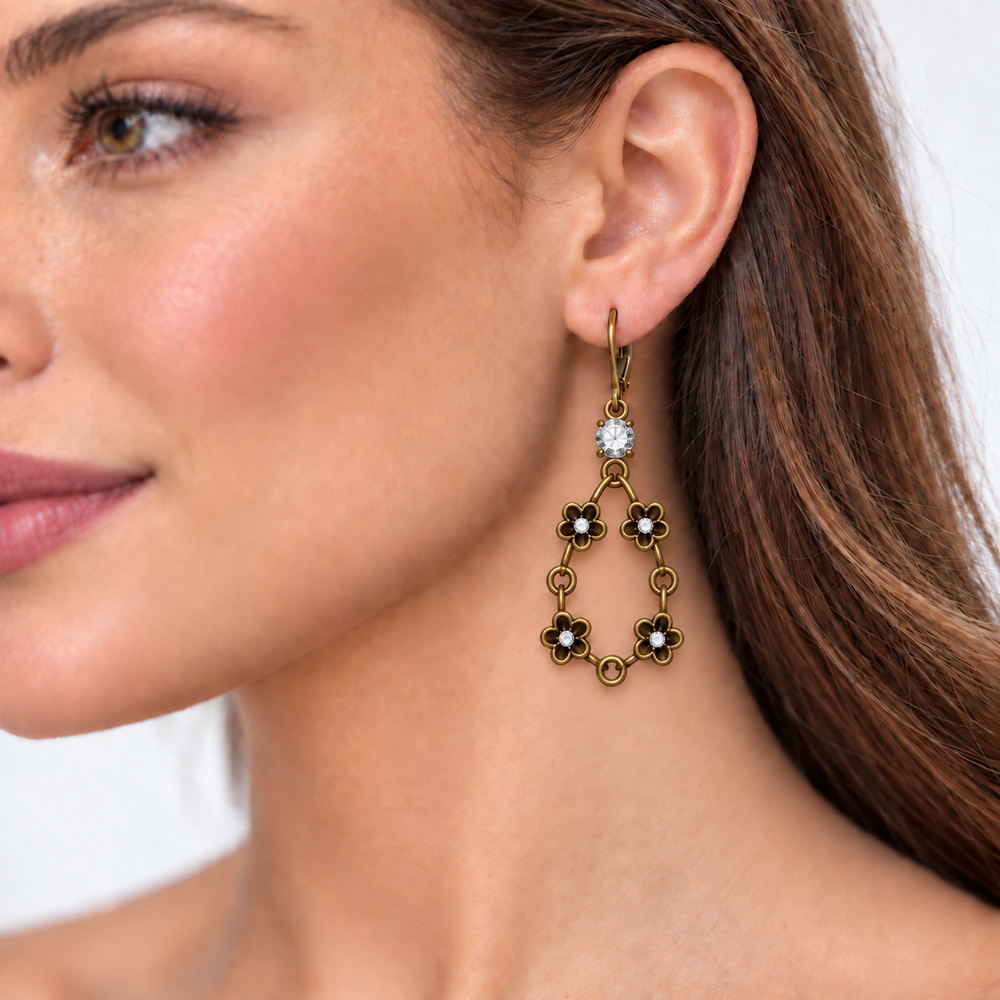 A close-up of a woman's ear wearing a dangling earring. The earring has an antique gold-tone finish with five flower-shaped links, each accented with small white pearls, and a clear round gemstone at the top.