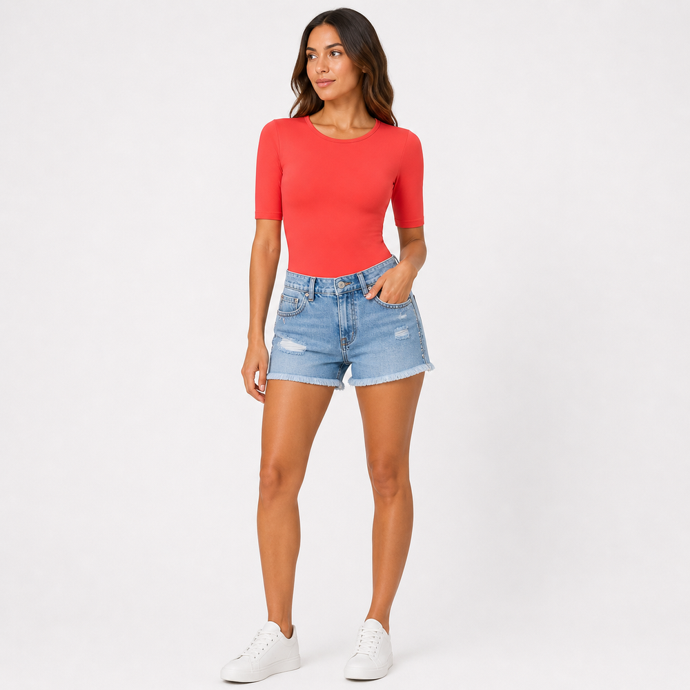 Woman wearing a bright coral top and denim shorts on a white background
