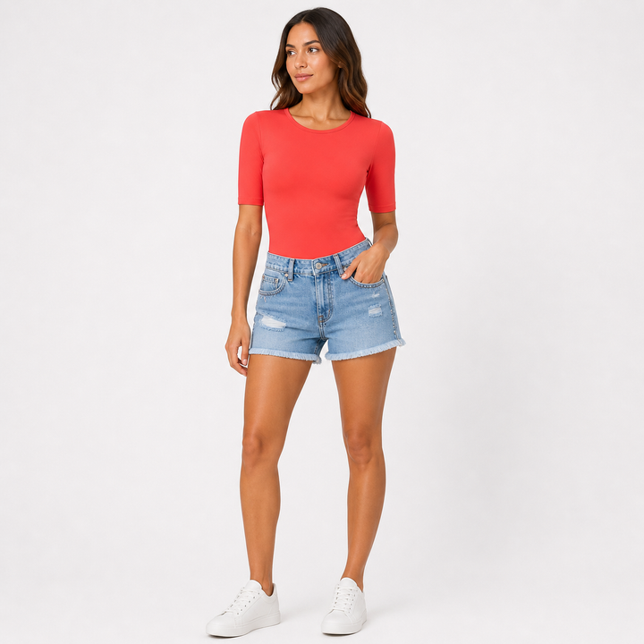 Woman wearing a bright coral top and denim shorts on a white background
