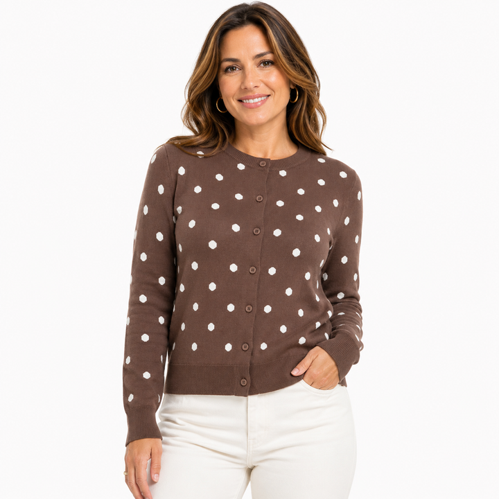 A woman modeling a brown long-sleeve cardigan sweater with white polka dots, paired with white pants, against a plain white background.