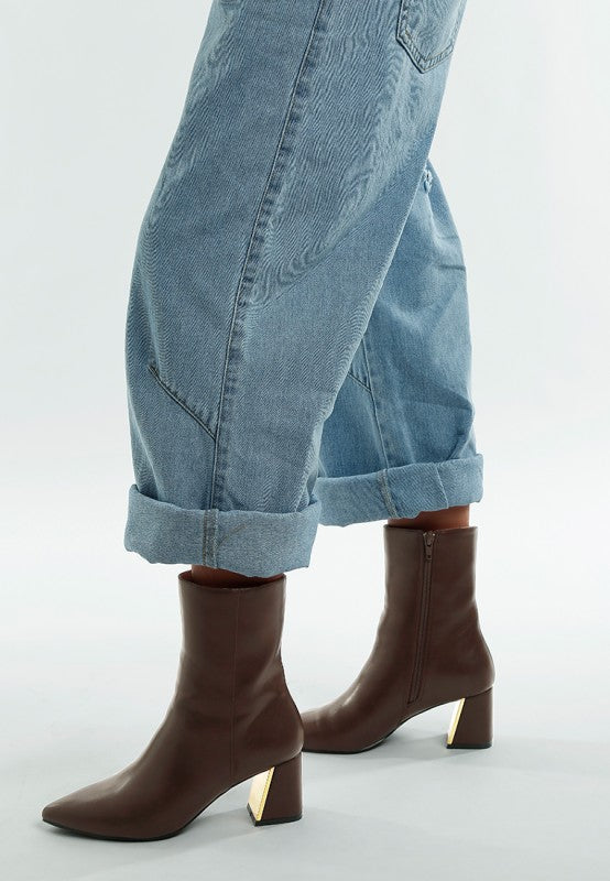 Brown ankle boots worn with rolled-up blue jeans on a light gray background