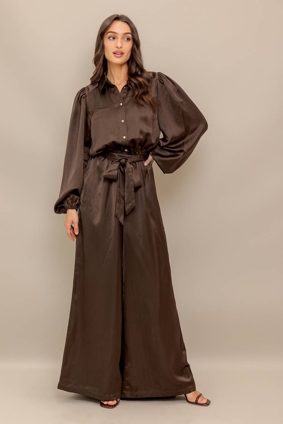 Woman wearing a brown jumpsuit with wide-leg pants on a beige background