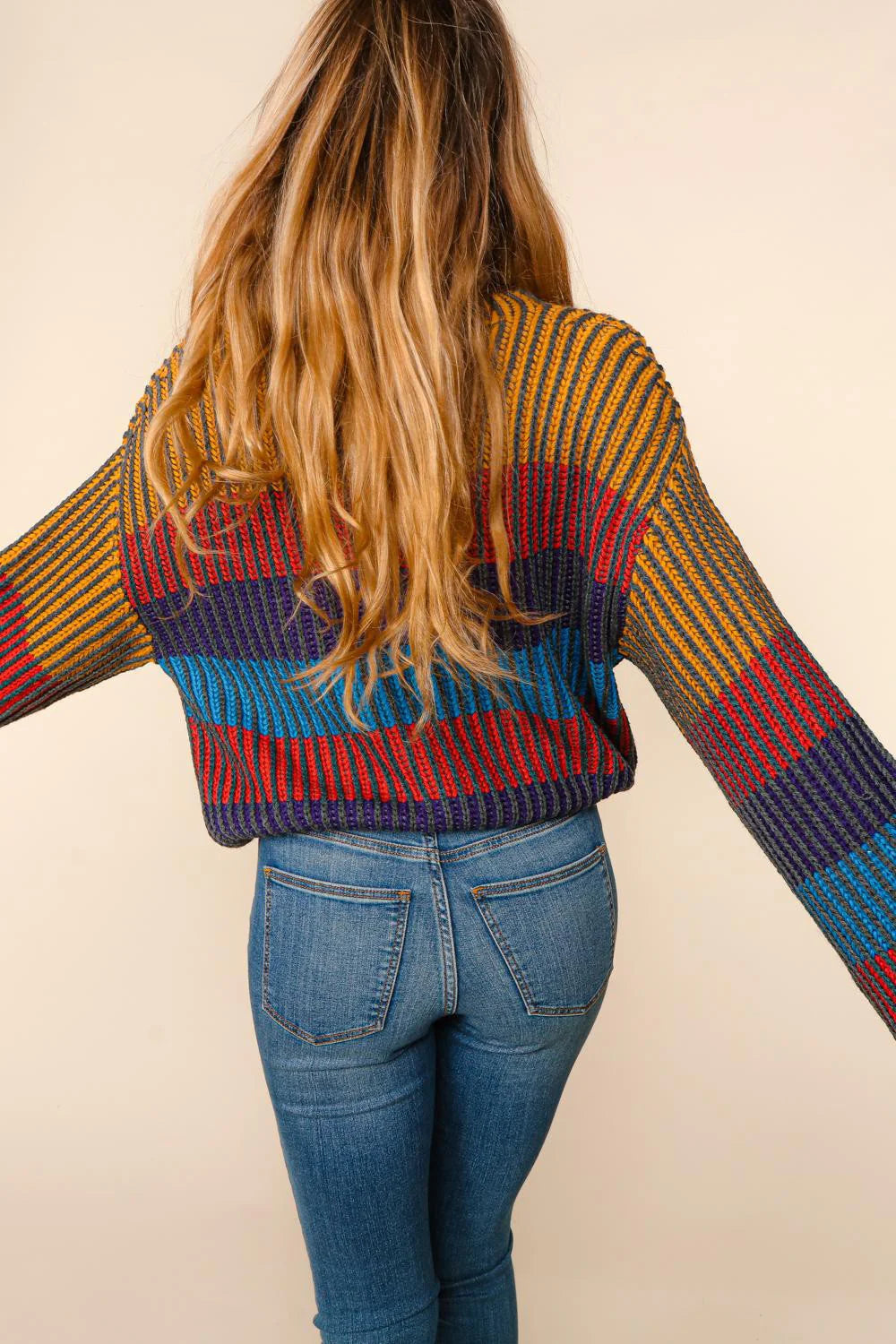 Person wearing a colorful striped sweater and blue jeans on a beige background