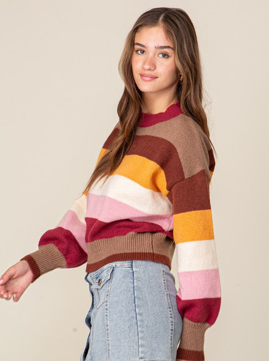 Woman wearing a colorful striped sweater and denim skirt against a plain background