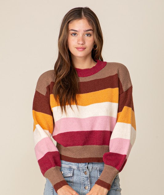 Woman wearing a colorful striped sweater and denim shorts on a beige background
