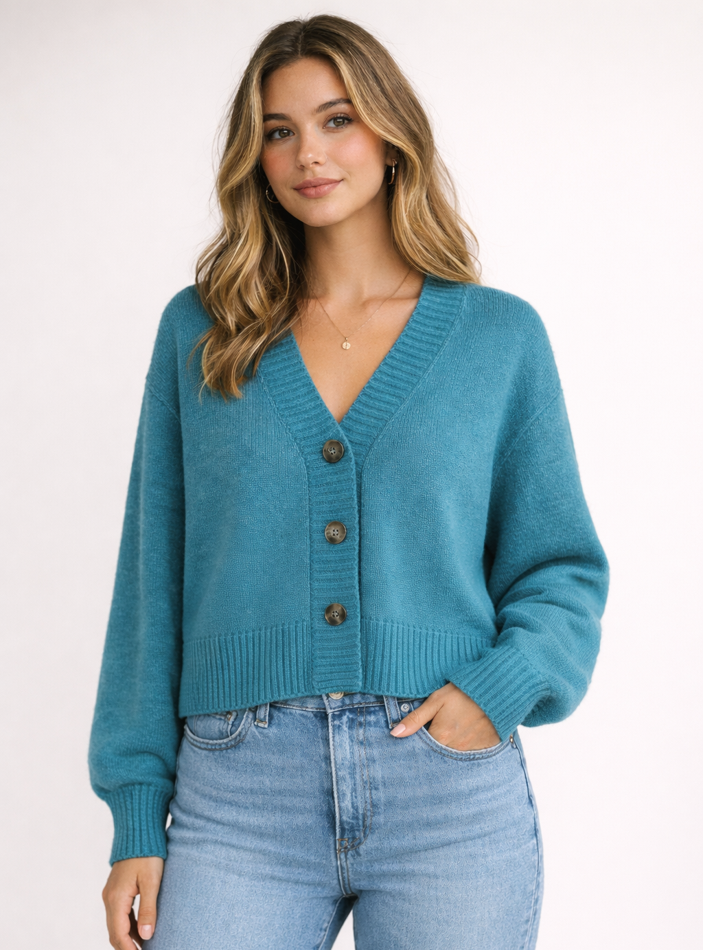 Woman wearing a teal cardigan and light blue jeans on a white background