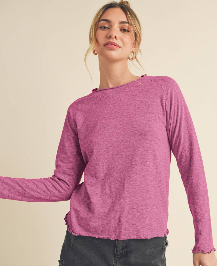 Woman wearing a berry long-sleeve top and black denim on a beige background