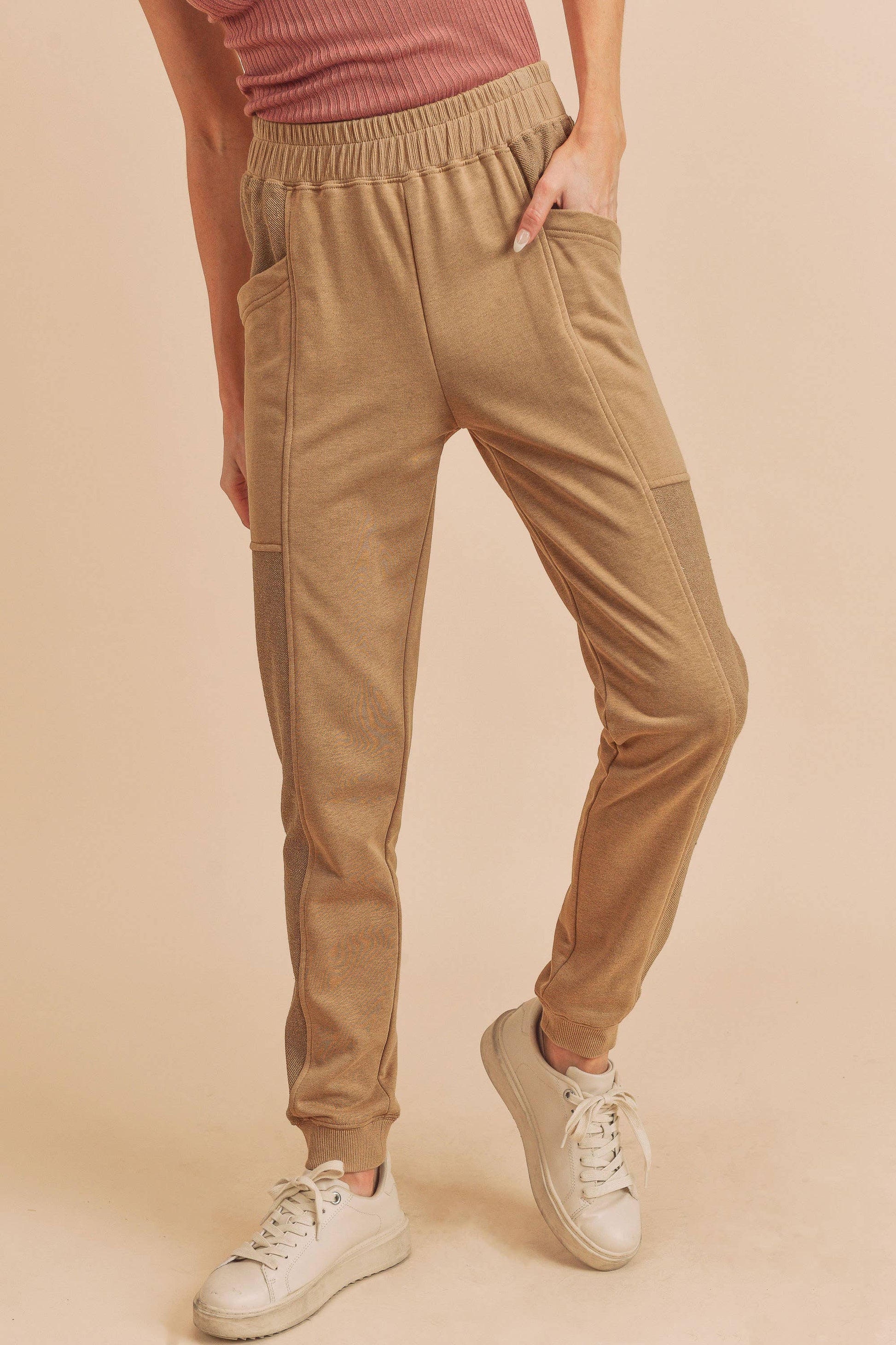 Person wearing beige jogger pants and white sneakers on a beige background