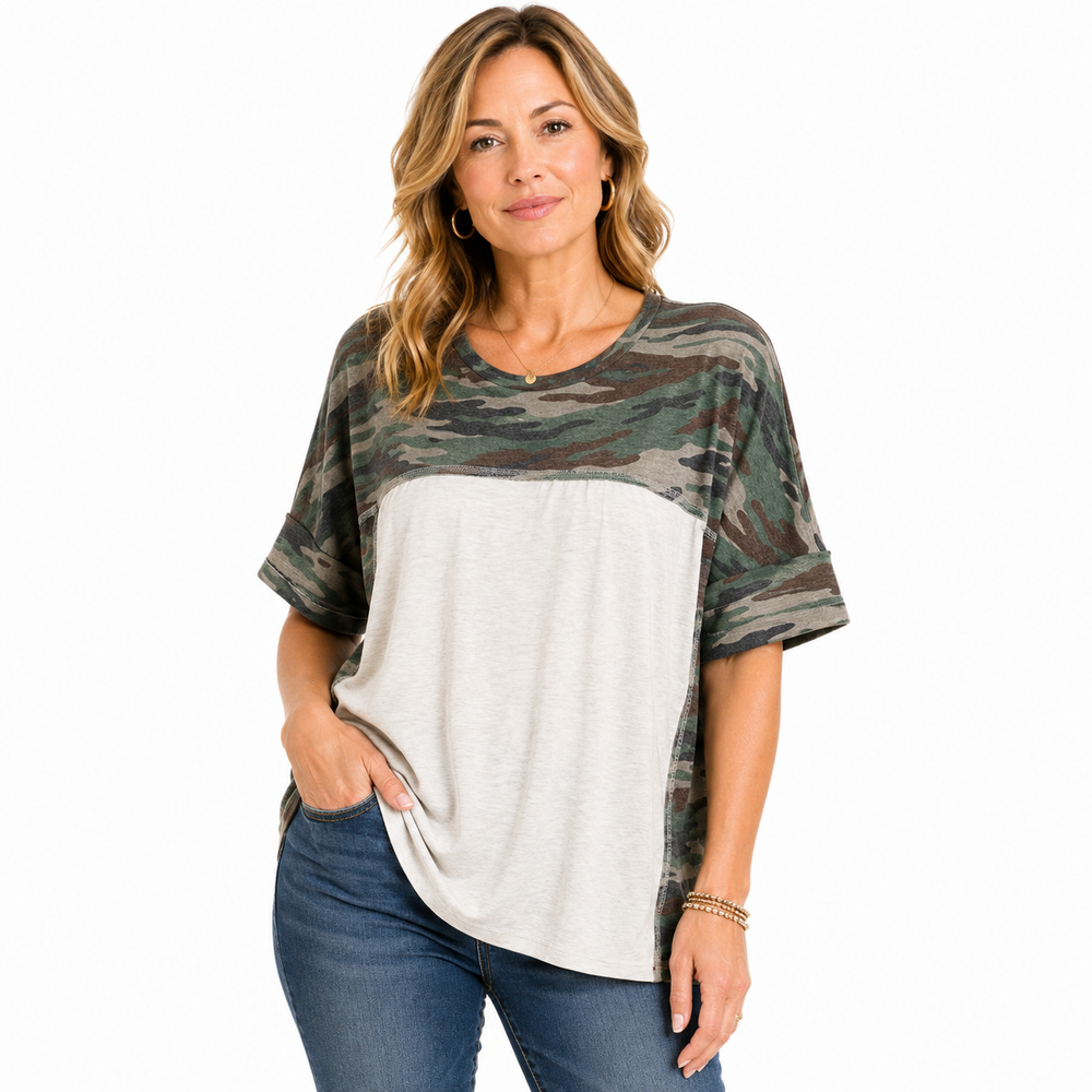 A woman modeling a short-sleeve colorblock top with a green and brown camouflage pattern on the upper portion and sleeves, and a light heather gray lower panel, paired with blue jeans against a white background.