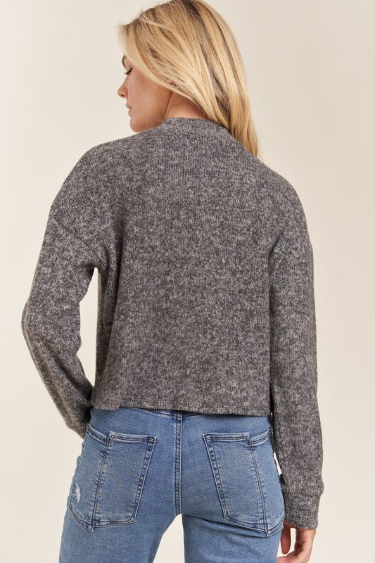 Person wearing a gray sweater and blue jeans on a beige background
