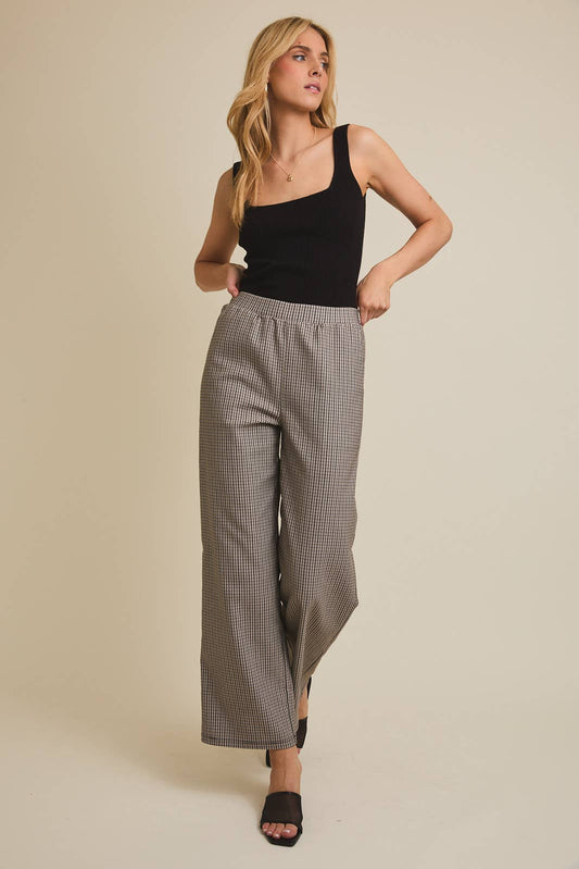 Woman wearing a black tank top and checkered pants against a beige background