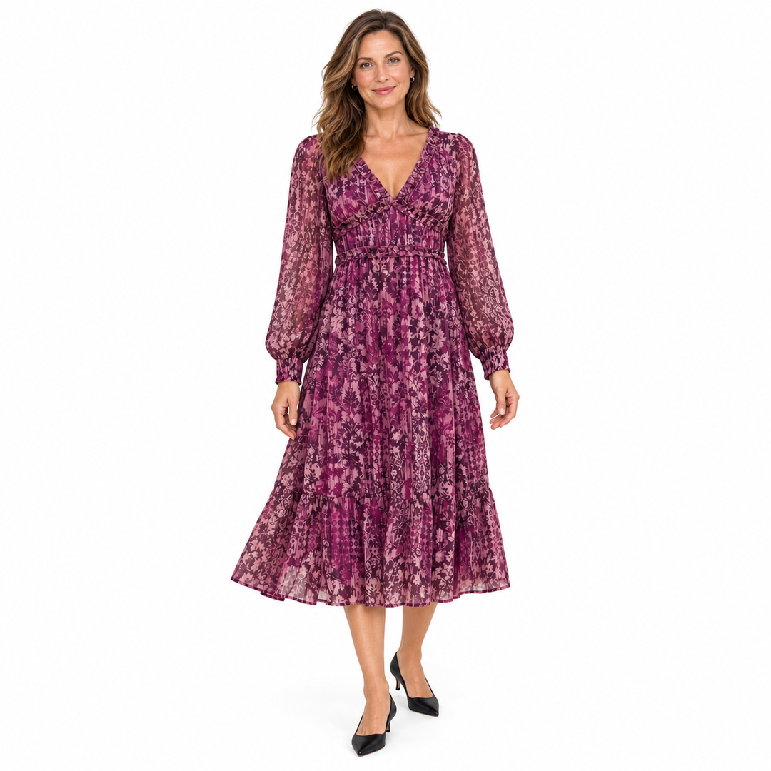 A woman modeling a long-sleeved midi dress with a purple and pink abstract floral pattern, featuring a V-neckline and a tiered skirt, set against a plain white background.