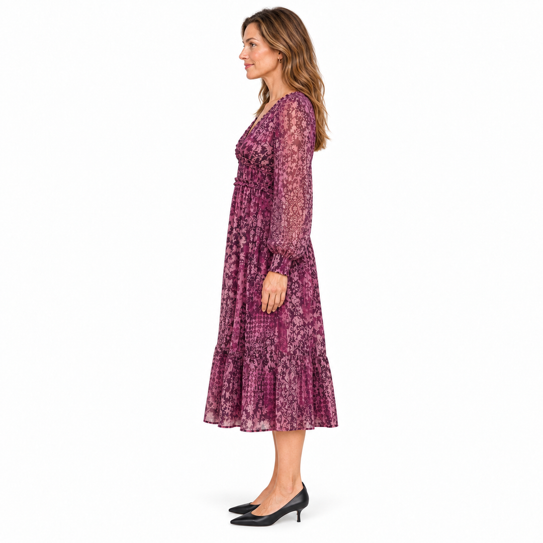 A woman modeling a long-sleeve midi dress with a purple and pink floral batik pattern, shown in profile against a solid white background.