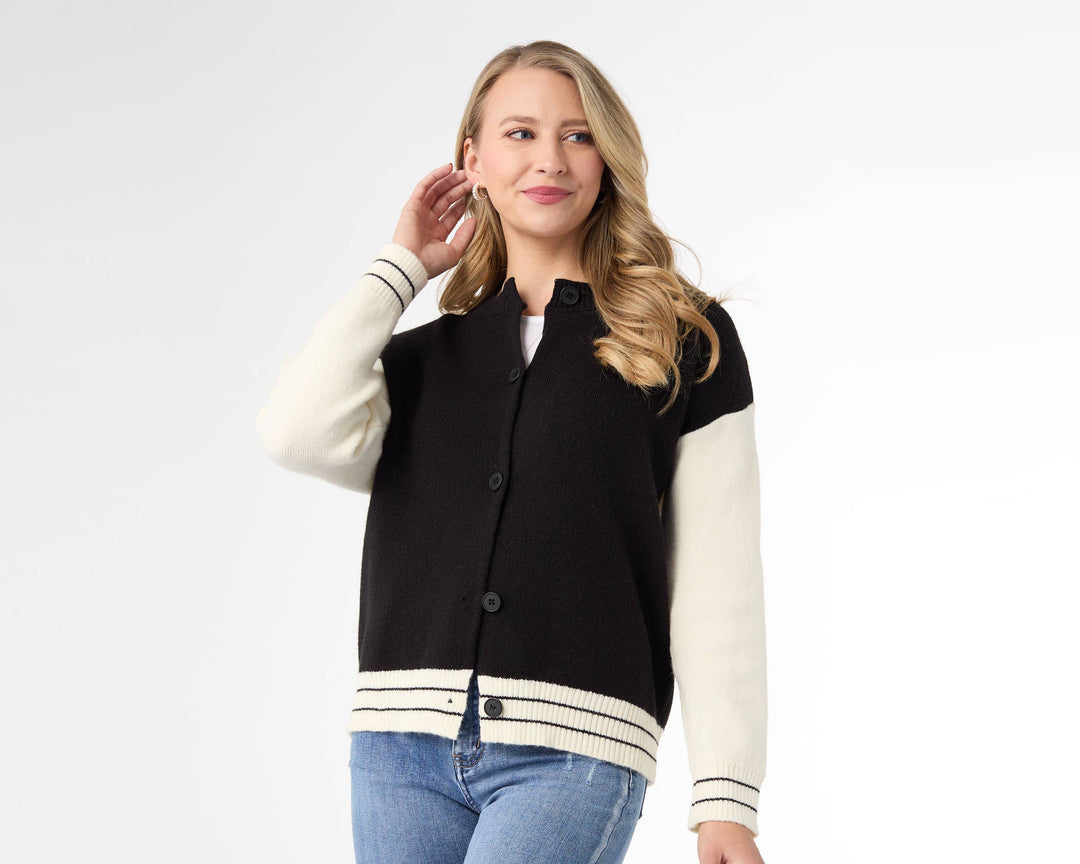 Woman wearing a black and white varsity jacket with blue jeans on a white background