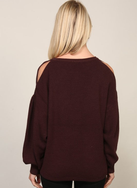 Woman wearing a burgundy sweater with cut-out shoulders against a beige background