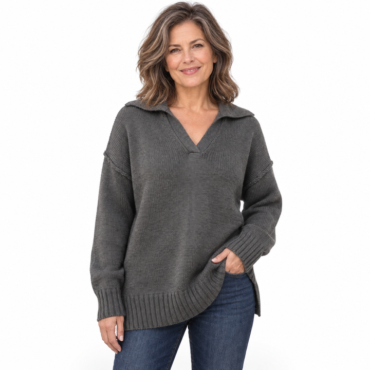 A woman wearing a dark gray ribbed knit sweater with a split V-neck collar and blue jeans, standing against a plain white background.