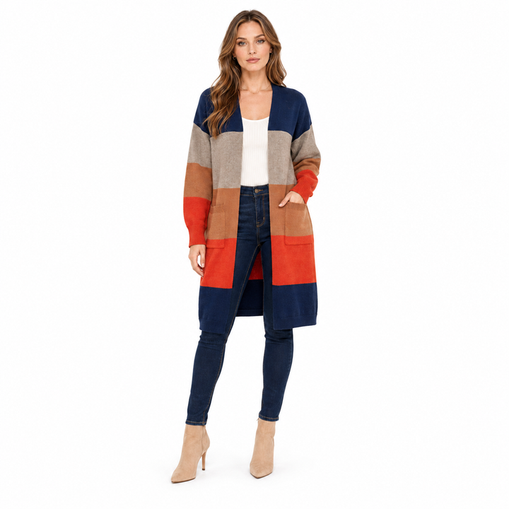 A woman modeling a long color-block knit cardigan with navy, beige, tan, and rust-orange panels, worn over a white top and dark blue skinny jeans against a plain white background.