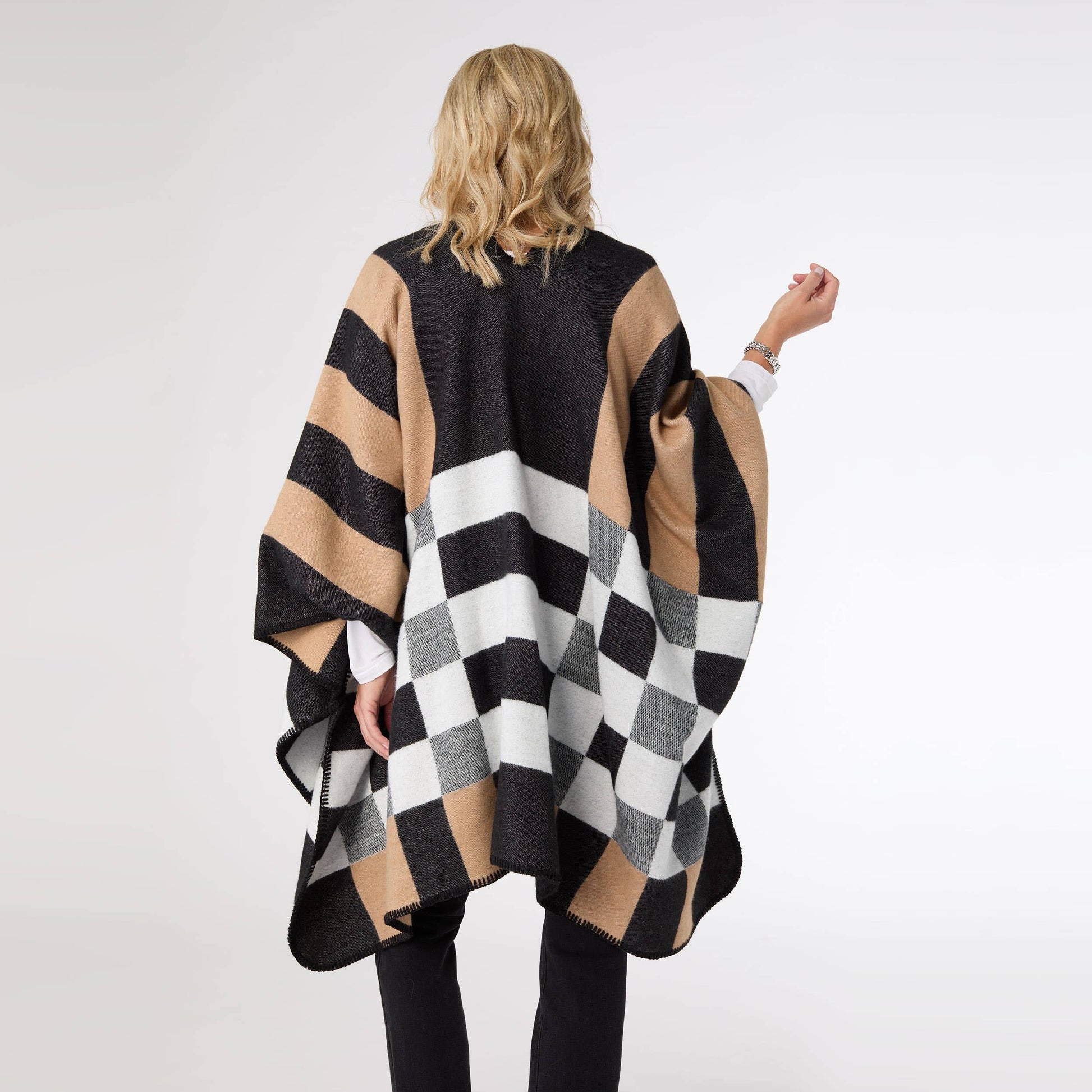 Person wearing a black, beige, and white checkered poncho on a white background