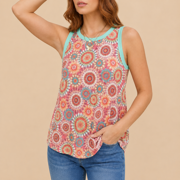 A woman wearing a sleeveless tank top with a colorful circular floral mandala pattern and light blue trim, paired with blue jeans, against a solid beige background.