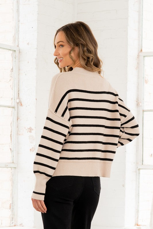 Woman wearing a cream and black striped sweater in front of a white window pane background