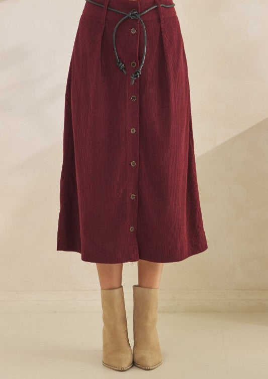 Maroon skirt with buttons and a tie waist, worn with beige boots on a neutral background