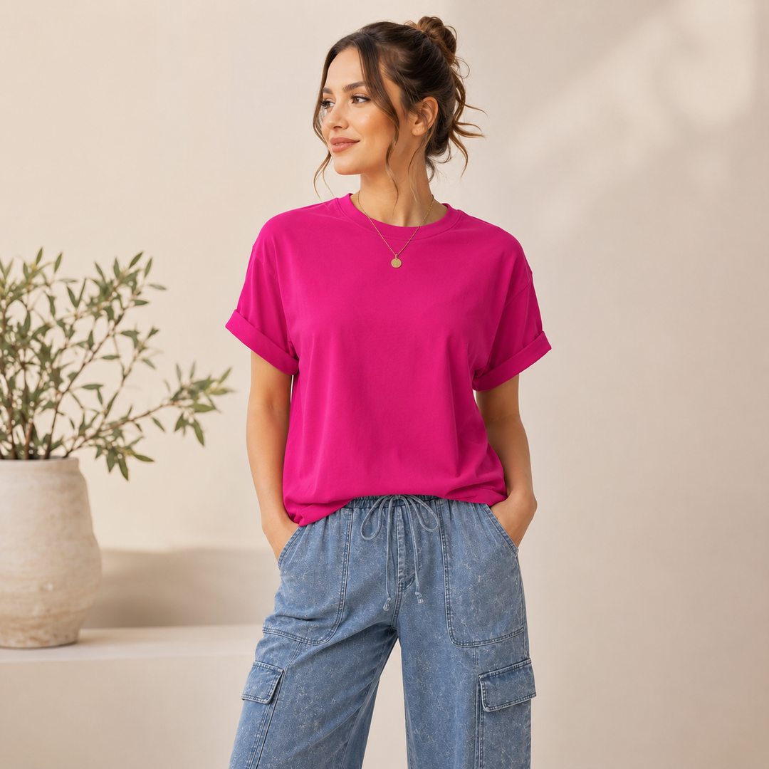 Woman wearing a bright pink t-shirt and blue cargo pants standing against a beige wall.